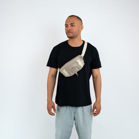 Mann trägt beige Bauchtasche 'Devin' von Johnny Urban quer über der Brust, schwarzes T-Shirt und helle Hose