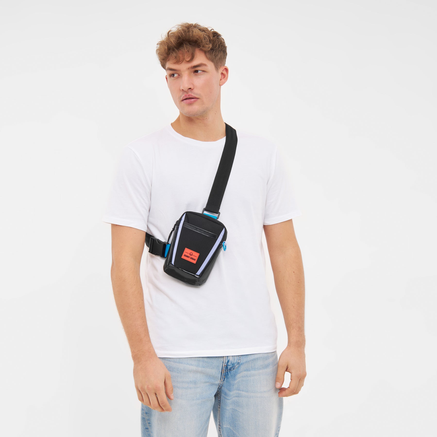 Mann trägt Umhängetasche 'Lex' in Schwarz mit reflektierenden Details und orangem Logo auf weißen T-Shirt und blauen Jeans