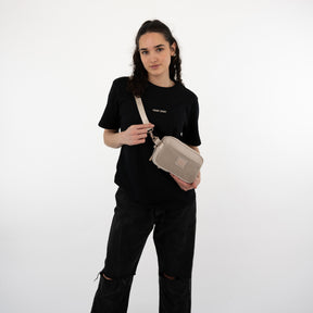 Frau trägt Umhängetasche 'Elliot' in Beige von Johnny Urban zur schwarzen T-Shirt und schwarzen Hose