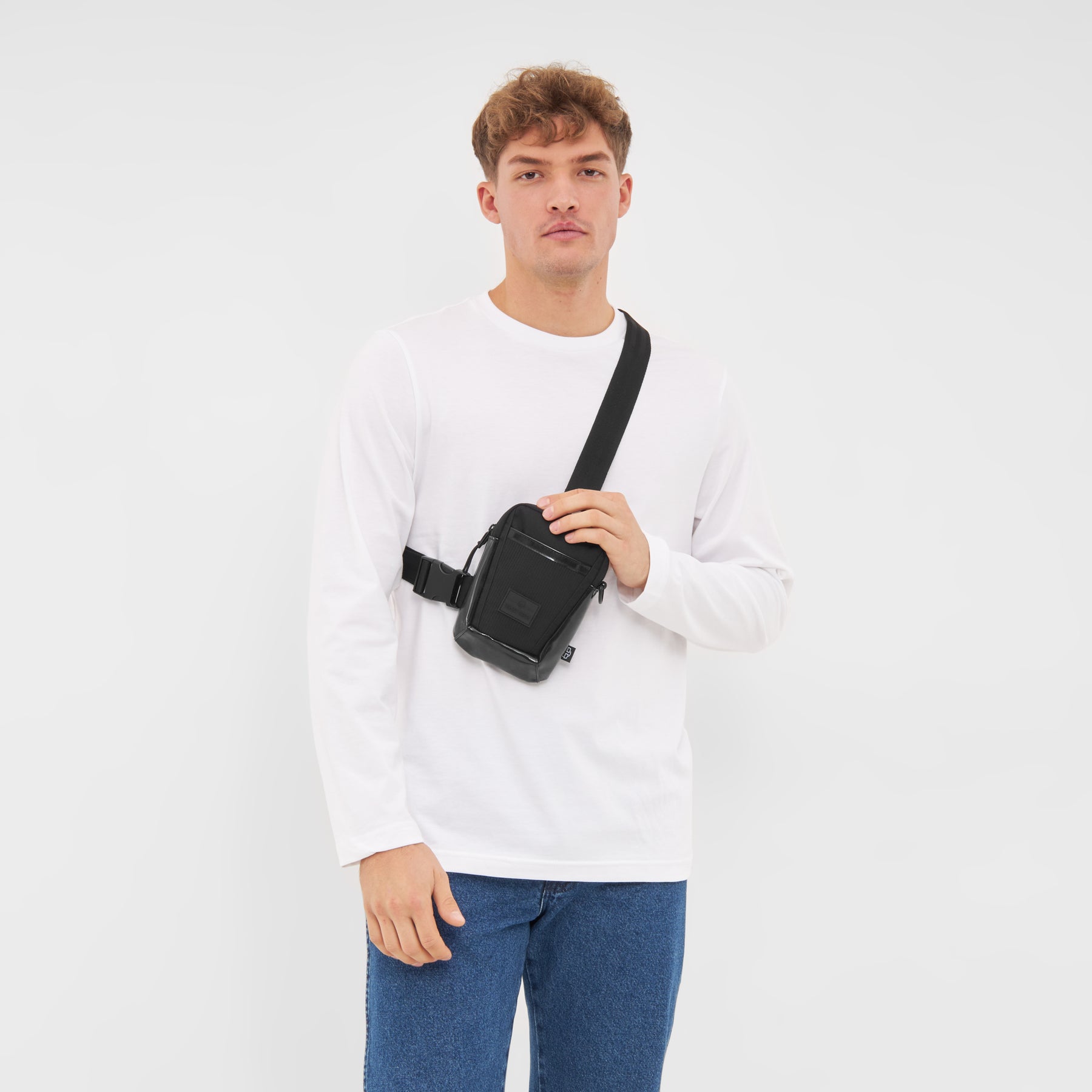 Mann mit weißem langärmligem Shirt und blauen Jeans trägt schwarze Johnny Urban Umhängetasche 'Lex' quer über den Oberkörper