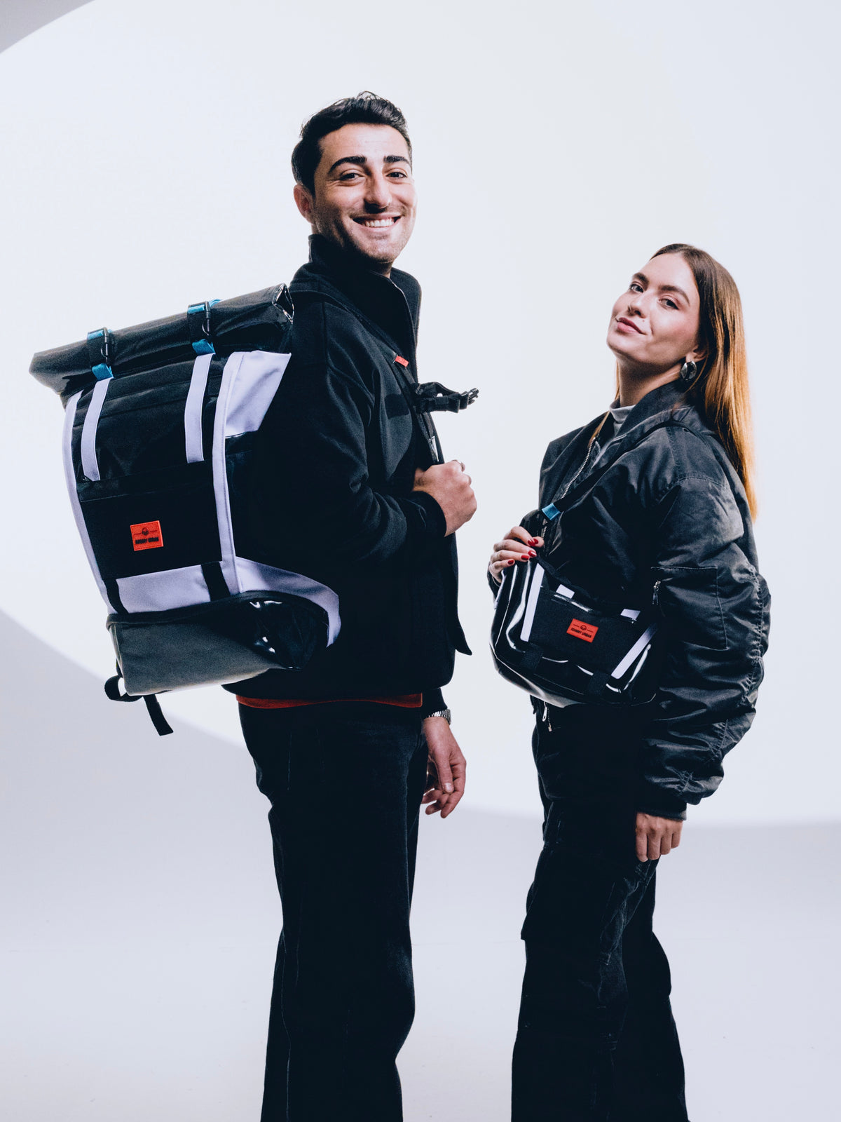 Ein Mann und eine Frau präsentieren ihre neuen Rucksäcke der Johnny Urban Edge Series mit reflektieren Eigenschaften. 