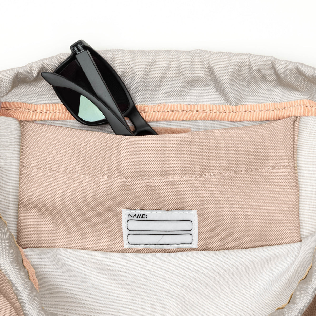 Innenfach des Kinder Turnbeutels 'Nino' mit beige Stoff und Namensfeld, schwarze Sonnenbrille steckt im Fach