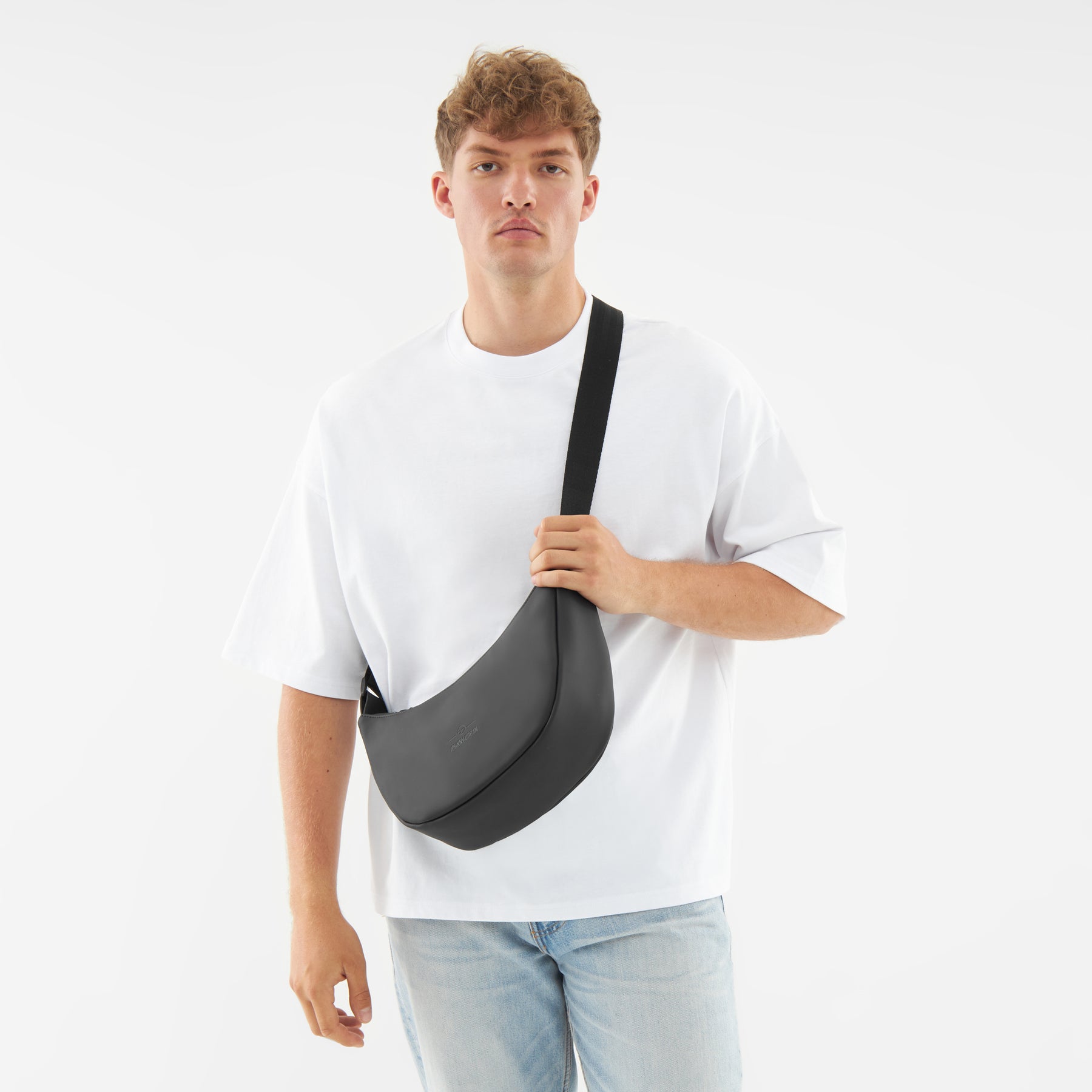 Mann trägt schwarze Half Moon Tasche „Rory“ von Johnny Urban quer über den Oberkörper, weiße T-Shirt, helle Jeans