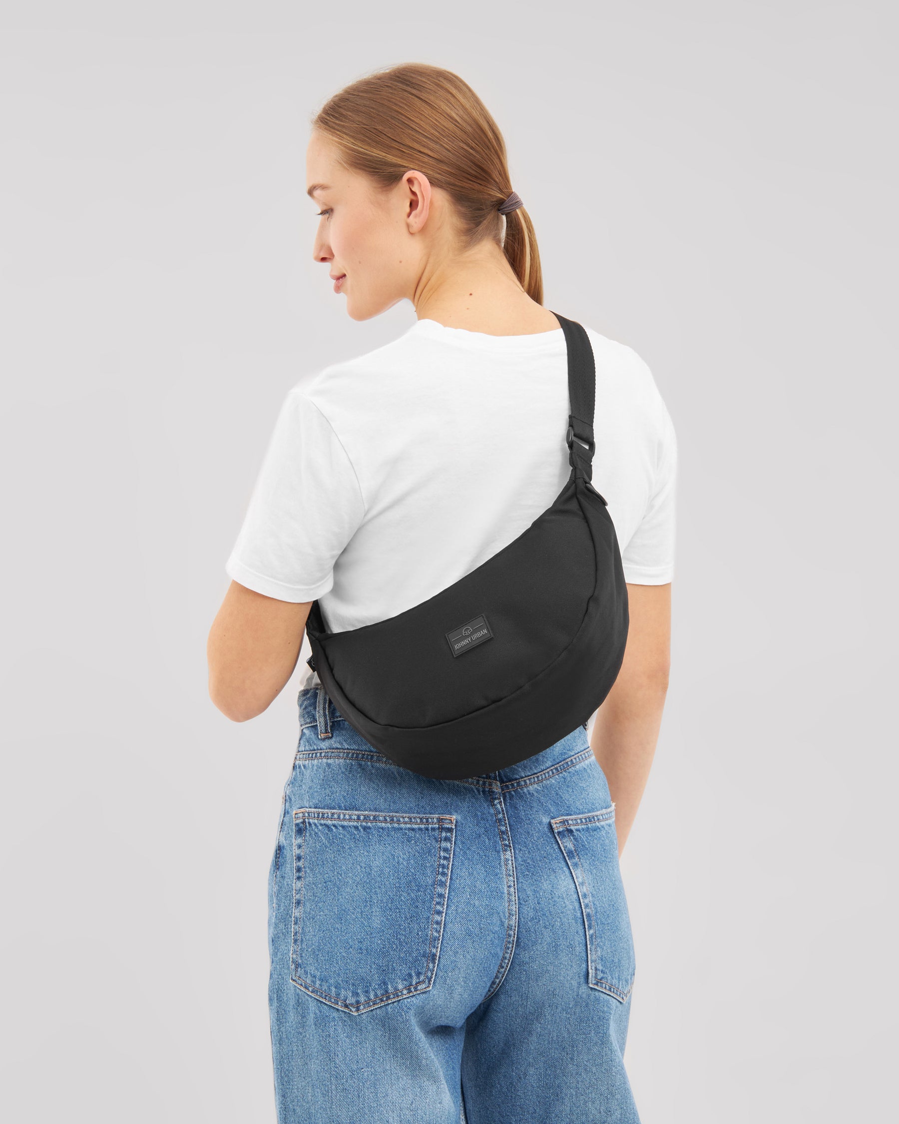 Frau von hinten mit schwarzer Half Moon Umhängetasche 'Ally Medium', weißem T-Shirt und blauen Jeans