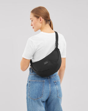 Frau von hinten mit schwarzer Half Moon Umhängetasche 'Ally Medium', weißem T-Shirt und blauen Jeans