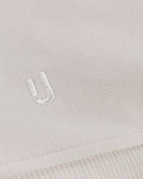 Nahaufnahme des cremefarbenen Oversized Crewnecks 'Carter' von Johnny Urban mit weißem gesticktem Logo