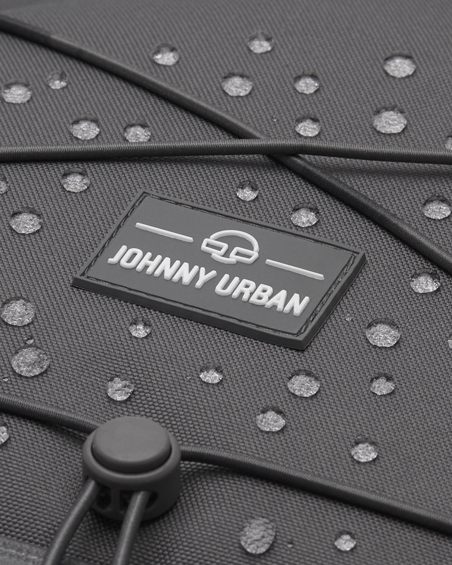 Nahaufnahme des grauen, wasserabweisenden Reiserucksacks 'Allen Large Travel' von Johnny Urban mit Wasserperlen auf der Oberfläche