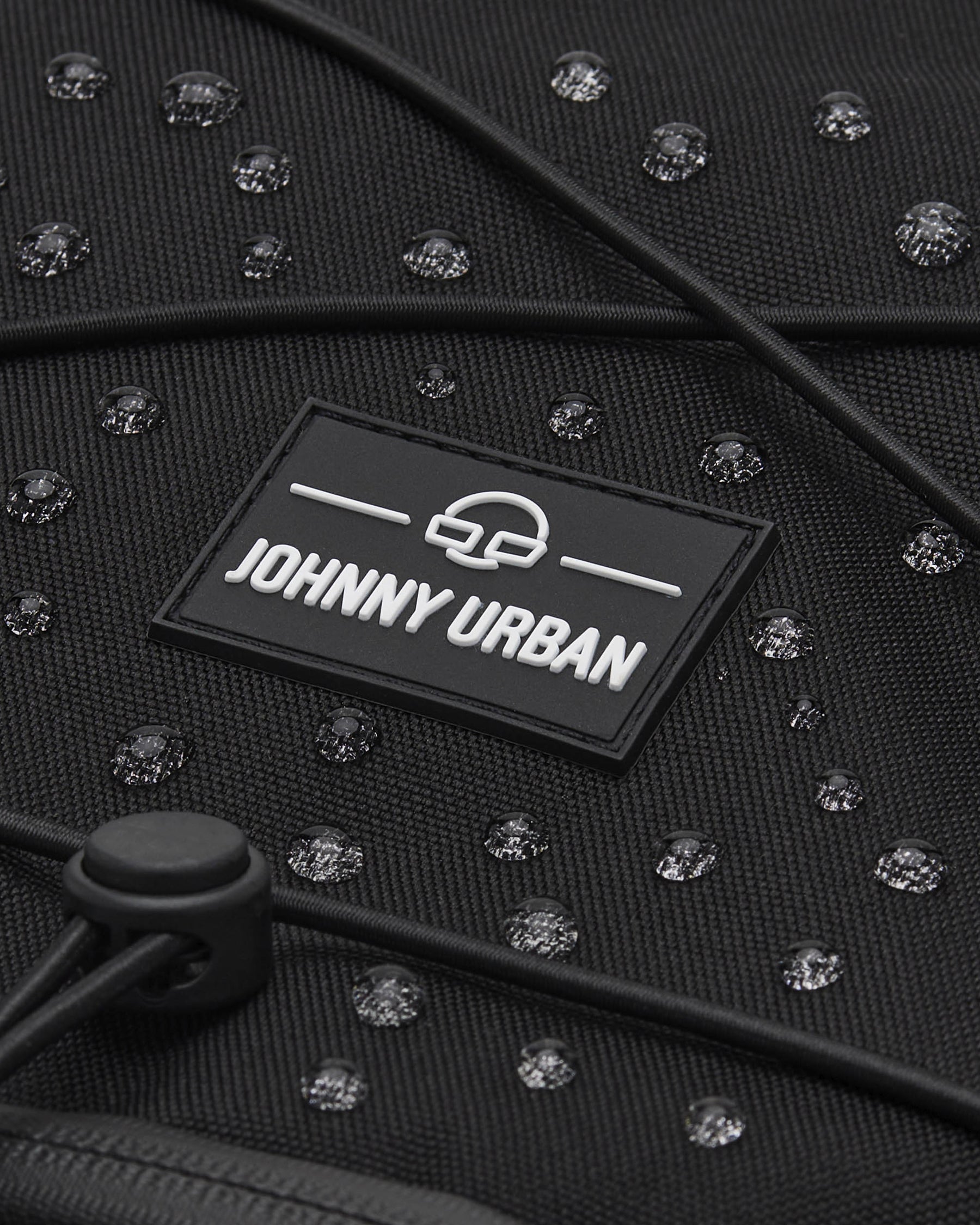 Nahe Aufnahme des schwarzen, wasserabweisenden Reiserucksacks Allen Large Travel von Johnny Urban mit sichtbaren Wassertropfen