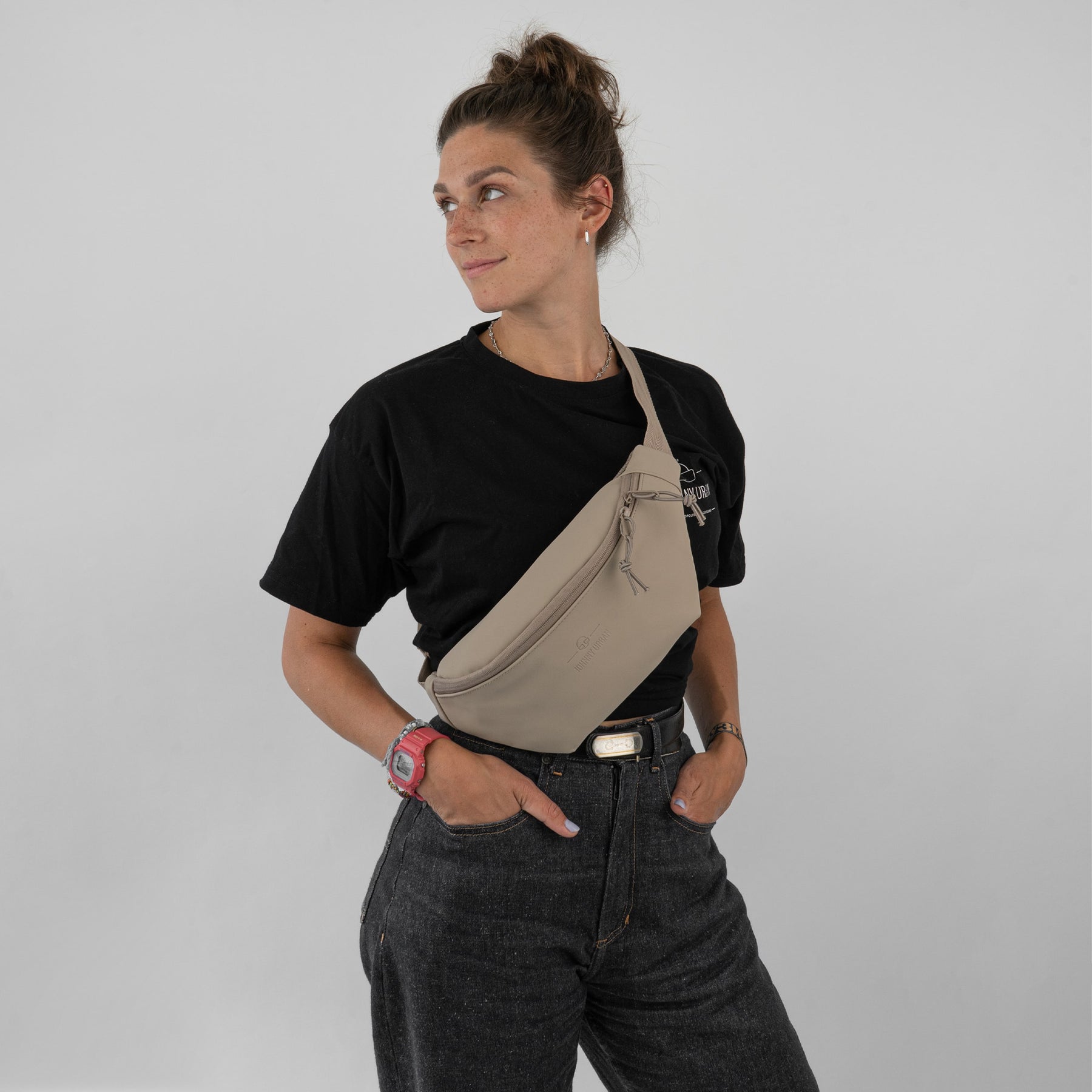 Frau trägt beige Bauchtasche 'Riley' von Johnny Urban quer über der Brust, schwarzes T-Shirt, dunkle Jeans