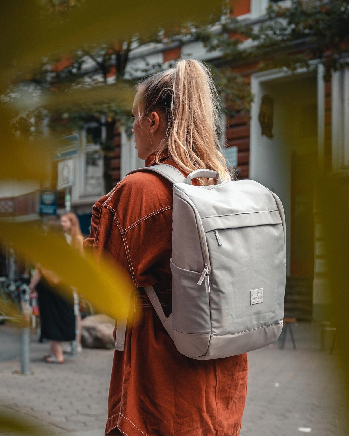 Frau mit Zopf trägt beigen Business Rucksack 'Jasper' von Johnny Urban auf dem Rücken in urbaner Umgebung