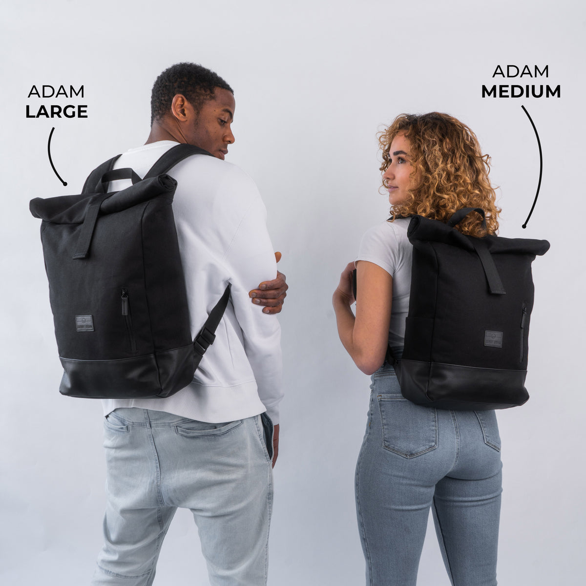 Zwei Personen tragen schwarze Rolltop-Rucksäcke Adam Large und Adam Medium, Größenvergleich