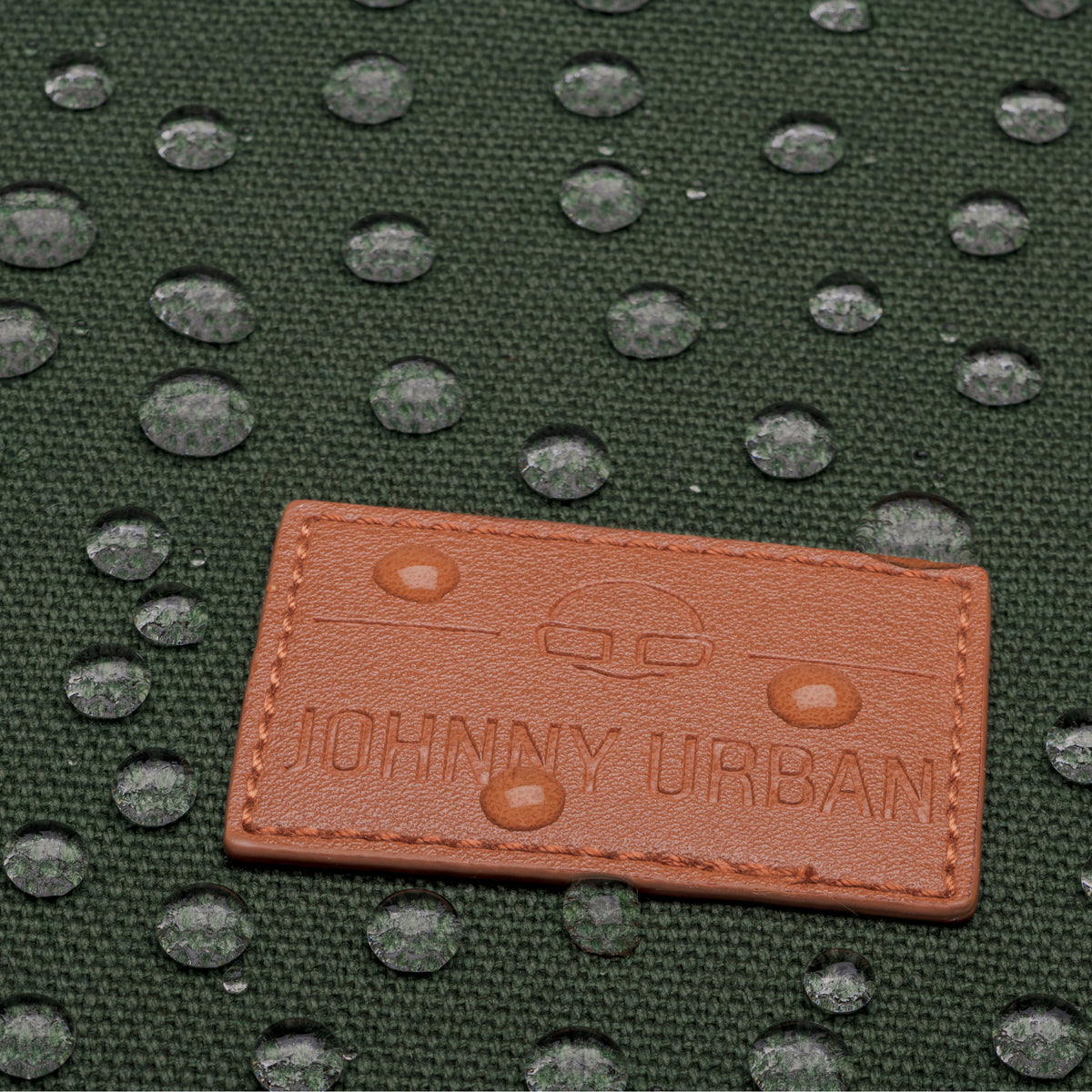 Wasserabweisendes grünes Canvas-Material mit braunem Johnny Urban Lederetikett und Wassertropfen