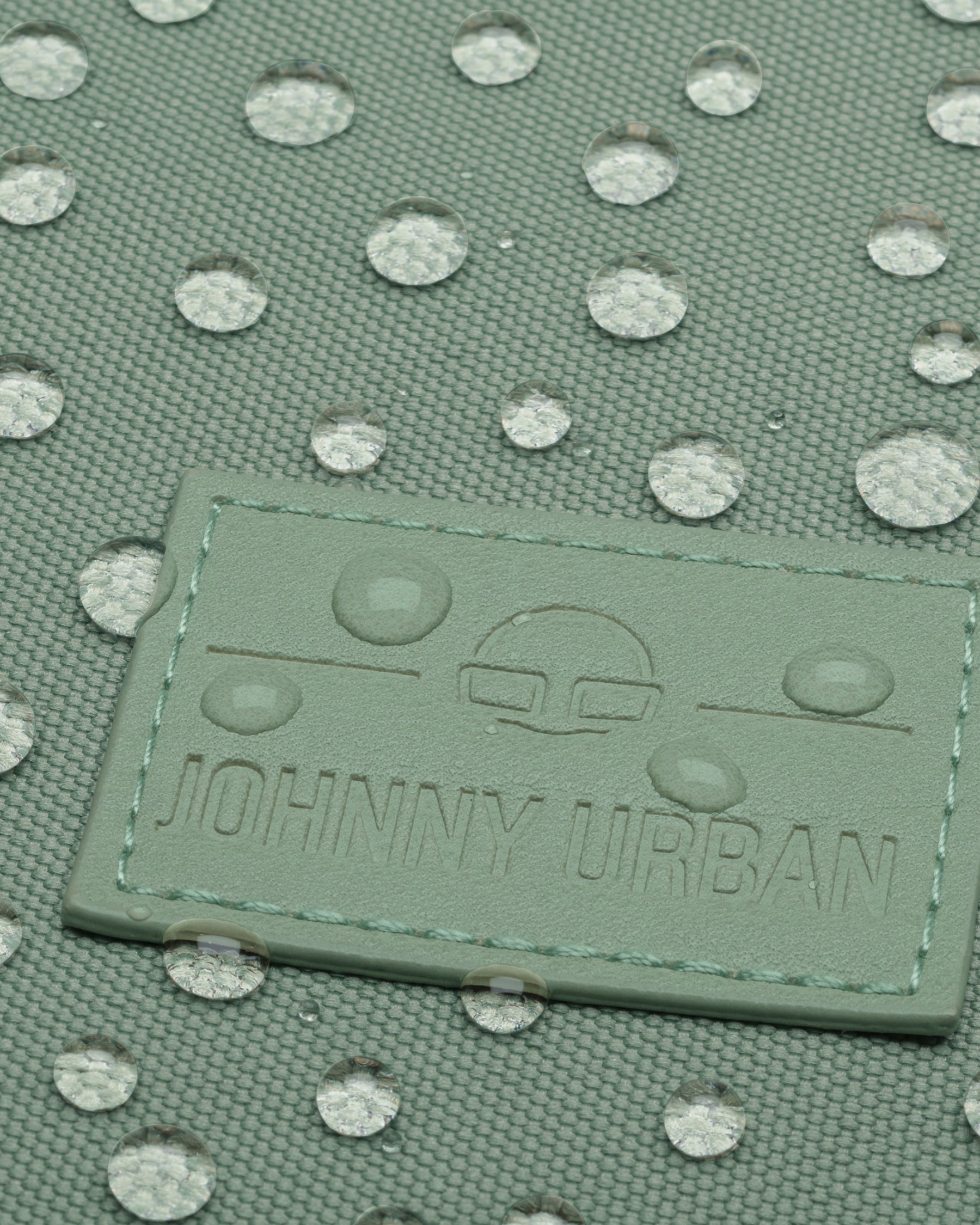 Nahaufnahme der wasserabweisenden Oberfläche und Markenprägung des Rucksacks 'Jona Small' von Johnny Urban